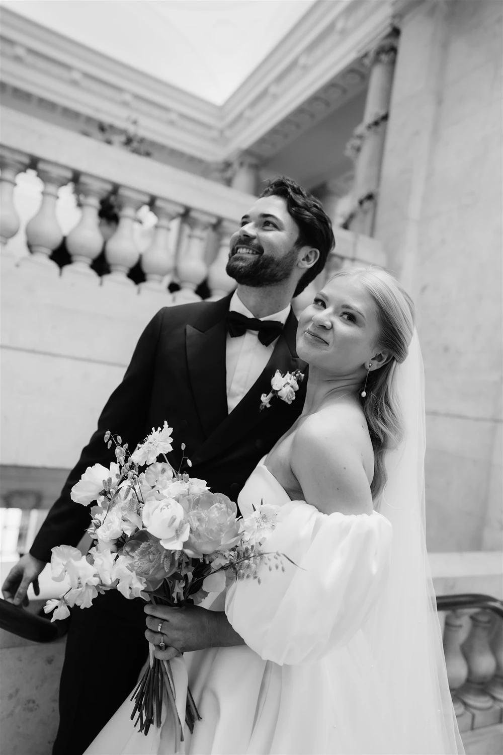 Black and white portrait of a smiling bride and groom holding a wedding bouquet.