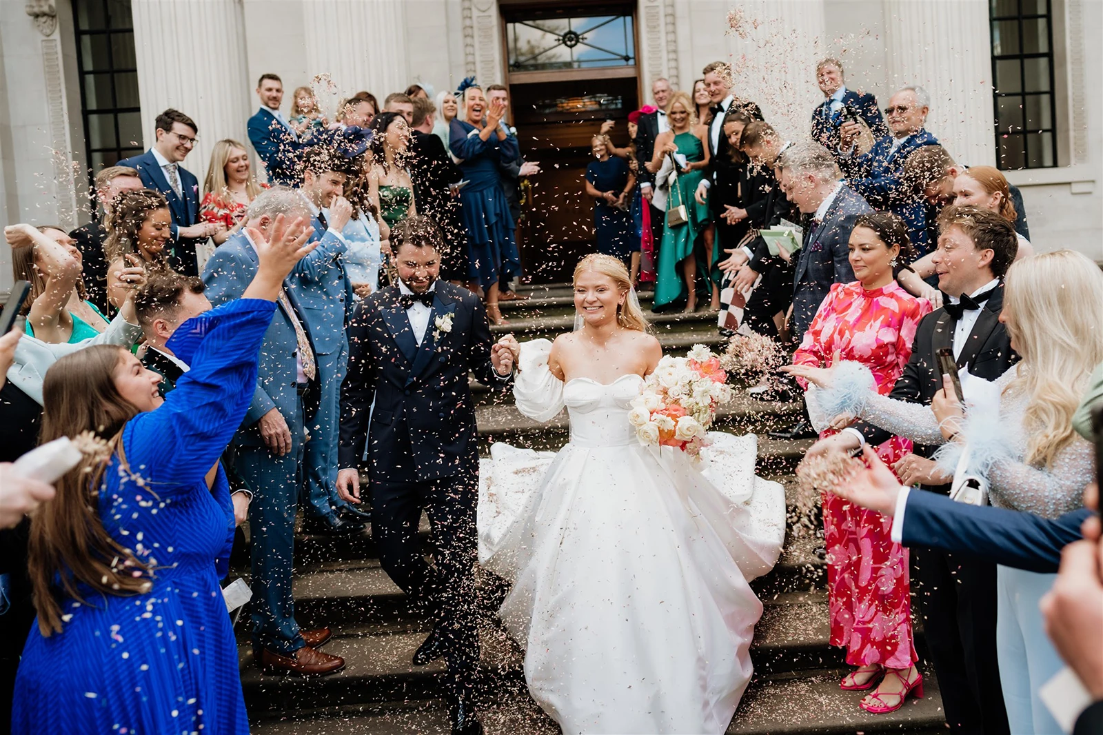 Newlywed couple walking through confetti thrown by guests outside The Old Marylebone Town Hall after the ceremony.