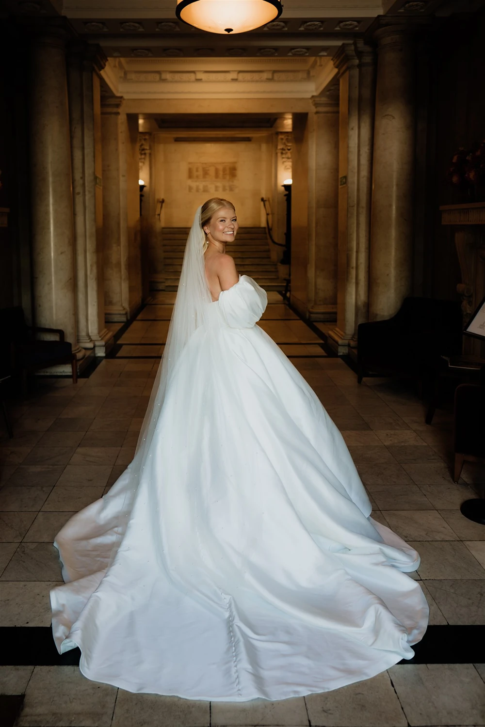 Bride smiling over her shoulder in a strapless wedding dress with long train inside The Old Marylebone Town Hall