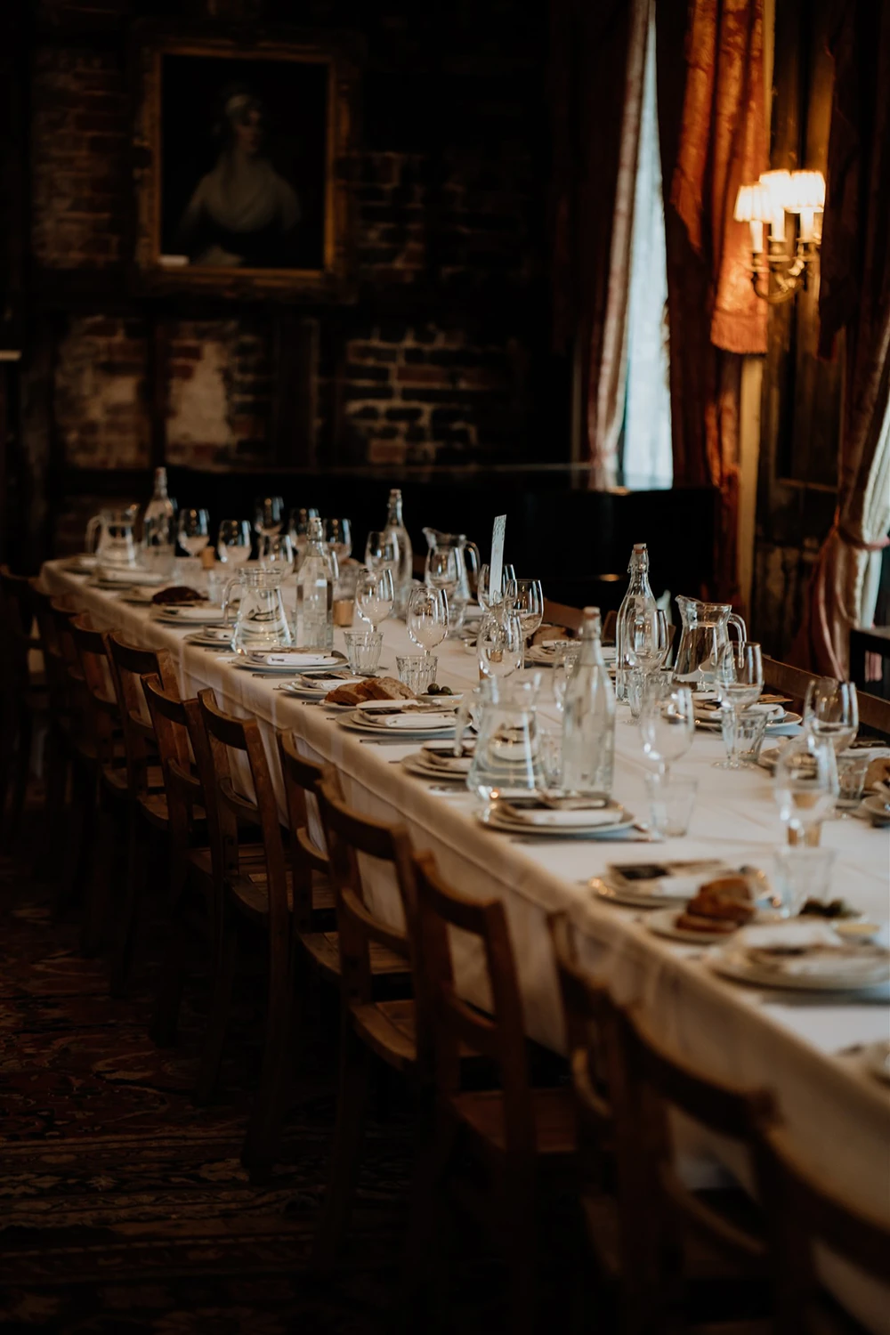 Long candlelit dining table prepared for a wedding reception with plates, bread, glasses and water carafes at Brunswick House