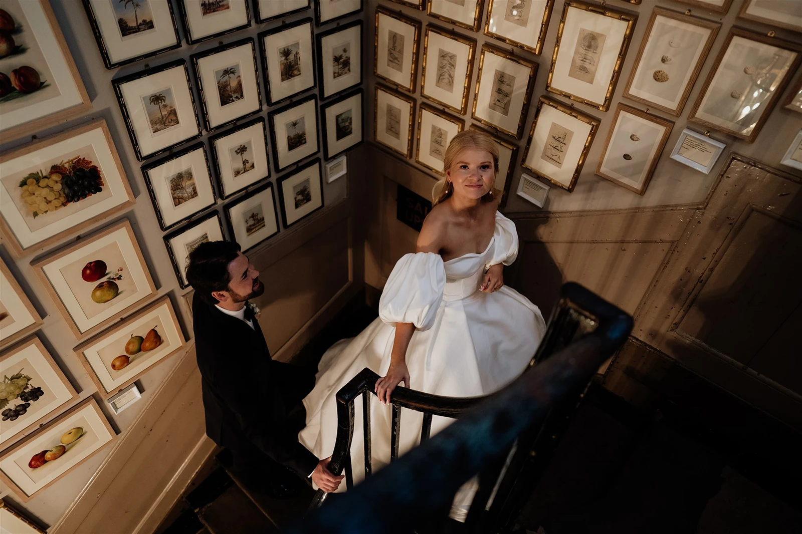 Bride and groom walking down a staircase lined with framed artwork Brunswick House Wedding