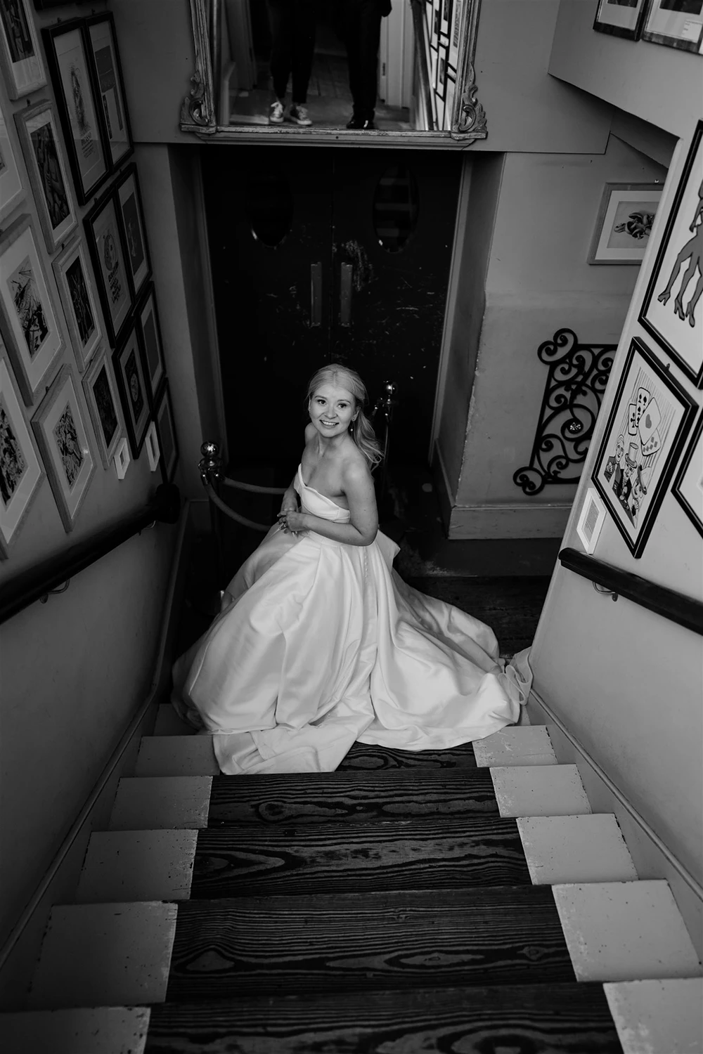 Black and white photo of a bride sitting on a staircase with her wedding dress spread across the steps.
