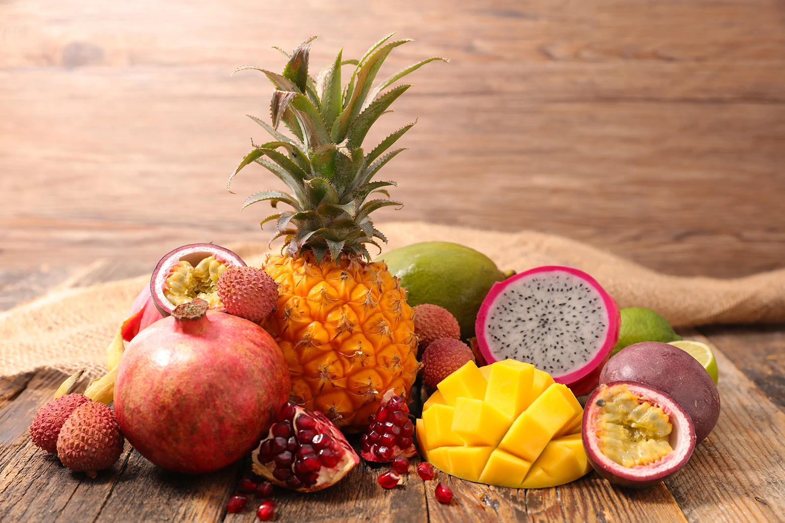 A selection of fresh tropical fruits, including pineapple, mango, passion fruit, pomegranate, lychee, dragon fruit, and lime, arranged on a rustic wooden table, showcasing vibrant colours and healthy eating.