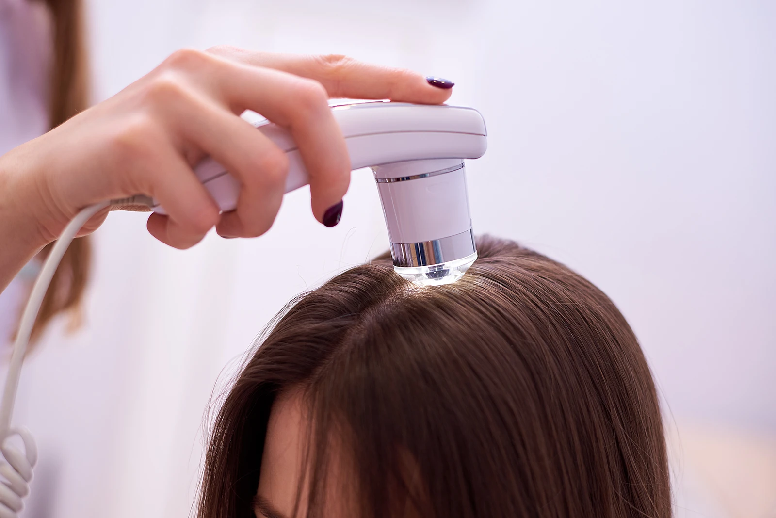 A specialist in multidisciplinary hair loss treatment uses a digital trichoscopy device with light to carefully examine the scalp and hair roots of a patient.